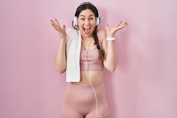 Poster - Young brunette woman wearing sportswear and headphones celebrating crazy and amazed for success with arms raised and open eyes screaming excited. winner concept