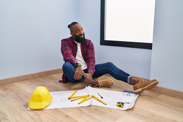 Sticker - African american man sitting on the floor at new home looking at blueprints looking away to side with smile on face, natural expression. laughing confident.