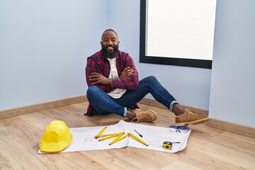 Poster - African american man sitting on the floor at new home looking at blueprints happy face smiling with crossed arms looking at the camera. positive person.