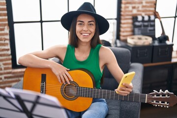 Canvas Print - Young hispanic woman musician using smartphone playing classical guitar at music studio