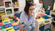 © Krakenimages.com - Young beautiful hispanic woman teacher sitting on table with stressed expression at kindergarten