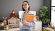 © Krakenimages.com - Young beautiful hispanic woman teacher holding books standing at kindergarten
