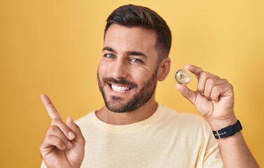 Sticker - Handsome hispanic man holding uniswap cryptocurrency coin smiling happy pointing with hand and finger to the side