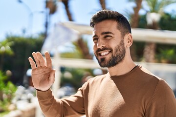 Young hispanic man smiling confident saying hello with hand at park