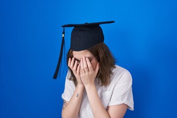 Sticker - Blonde caucasian woman wearing graduation cap with sad expression covering face with hands while crying. depression concept.