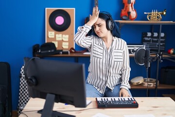 Poster - Young modern girl with blue hair at music studio wearing headphones surprised with hand on head for mistake, remember error. forgot, bad memory concept.