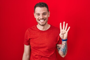 Poster - Young hispanic man standing over red background showing and pointing up with fingers number four while smiling confident and happy.