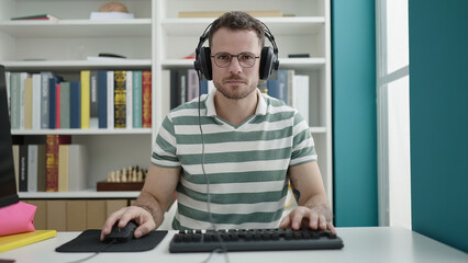 Wall Mural - Young caucasian man using computer wearing headphones at library university