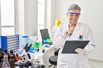 Poster - Middle age woman wearing scientist uniform writing on clipboard at laboratory