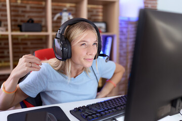 Poster - Young caucasian woman playing video games wearing headphones suffering of backache, touching back with hand, muscular pain