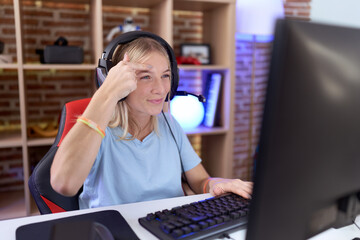 Canvas Print - Young caucasian woman playing video games wearing headphones pointing unhappy to pimple on forehead, ugly infection of blackhead. acne and skin problem