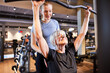 © Flamingo Images - gym instructor helping a senior woman lifting weights. Trainer helping a smiling senior lift weights. Senior woman exercising with personal trainer