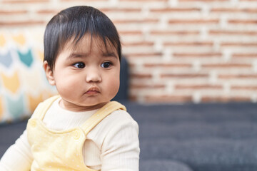 Sticker - Adorable hispanic baby sitting on sofa with relaxed expression at home