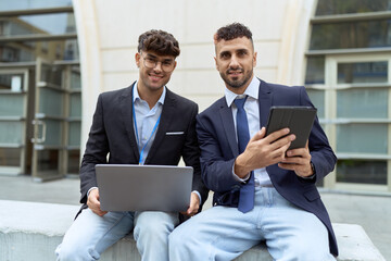 Wall Mural - Two hispanic men business workers using touchpad and laptop working at street