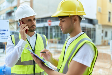 Wall Mural - Two hispanic men architects writing on document talking on smartphone at street