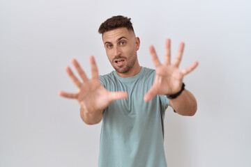 Hispanic man with beard standing over white background afraid and terrified with fear expression stop gesture with hands, shouting in shock. panic concept.