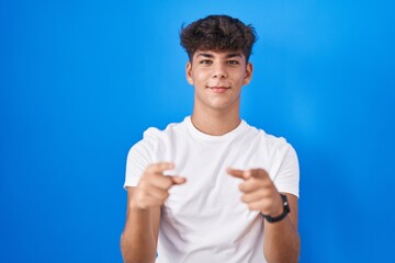 Wall Mural - Hispanic teenager standing over blue background pointing fingers to camera with happy and funny face. good energy and vibes.