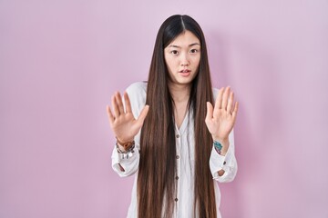 Poster - Chinese young woman standing over pink background moving away hands palms showing refusal and denial with afraid and disgusting expression. stop and forbidden.