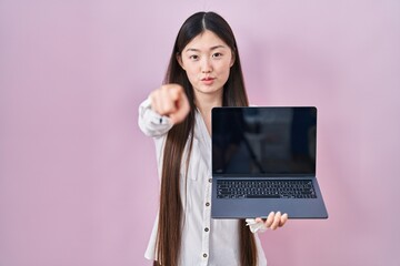 Poster - Chinese young woman holding laptop showing screen pointing with finger to the camera and to you, confident gesture looking serious