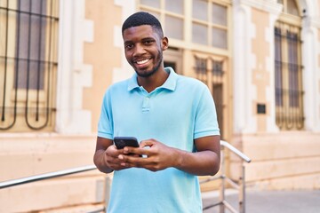 Wall Mural - Young african american man smiling confident using smartphone at street