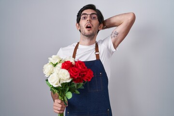 Poster - Young hispanic man holding bouquet of white and red roses crazy and scared with hands on head, afraid and surprised of shock with open mouth