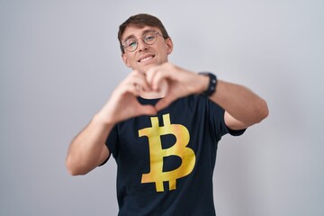 Sticker - Caucasian blond man wearing bitcoin t shirt smiling in love doing heart symbol shape with hands. romantic concept.