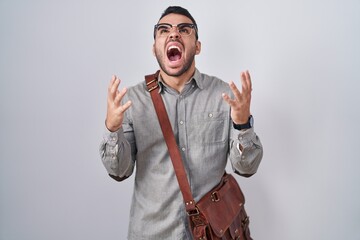 Canvas Print - Young hispanic man wearing suitcase crazy and mad shouting and yelling with aggressive expression and arms raised. frustration concept.