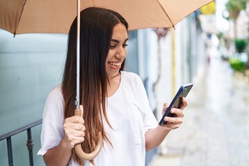 Poster - Young beautiful arab woman using smartphone holding umbrella at street