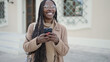 © Krakenimages.com - African woman smiling using smartphone at street