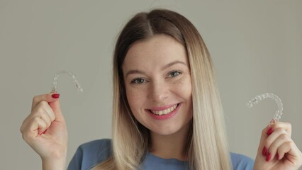 Wall Mural - The woman is smiling and holding a transparent plastic aligner for bite correction