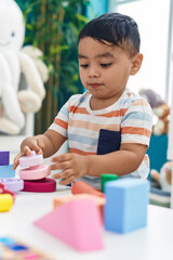 Wall Mural - Adorable hispanic toddler playing with construction blocks standing at kindergarten