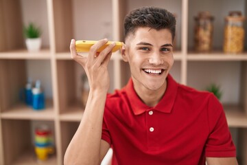 Wall Mural - Young hispanic man listening audio message sitting on table at home