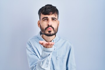 Canvas Print - Young hispanic man with beard standing over blue background looking at the camera blowing a kiss with hand on air being lovely and sexy. love expression.