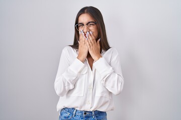 Canvas Print - Young brunette woman wearing glasses laughing and embarrassed giggle covering mouth with hands, gossip and scandal concept