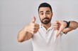 © Krakenimages.com - Young hispanic man with beard wearing casual clothes over white background doing thumbs up and down, disagreement and agreement expression. crazy conflict