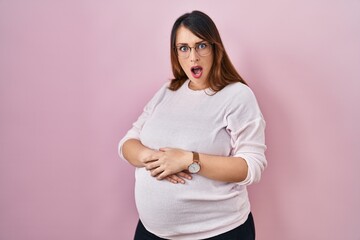 Canvas Print - Pregnant woman standing over pink background in shock face, looking skeptical and sarcastic, surprised with open mouth