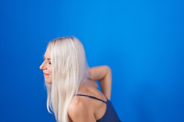 Poster - Caucasian woman standing over blue background suffering of backache, touching back with hand, muscular pain