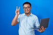© Krakenimages.com - Chinese young man using computer laptop smiling with happy face winking at the camera doing victory sign with fingers. number two.