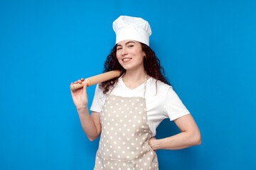 Wall Mural - girl chef in uniform holds items for cooking and smiles on blue background, portrait of girl housewife