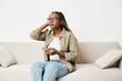 © SHOTPRIME STUDIO - African American woman business freelancer working sitting on the couch at home in the phone, business calls and messages happiness smile, home clothes and eyeglasses, light interior background.