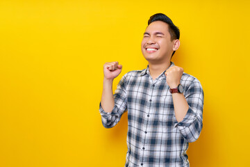 excited young handsome asian man celebrating victory and raised fists isolated on yellow background.