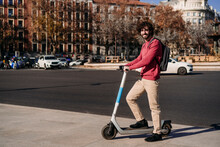 Smiling Young Man Standing With Electric Push Scooter On Footpath