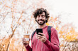 © Westend61 - Happy man using mobile phone and holding coffee cup standing at footpath