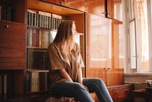 Young Woman Sitting By Bookshelf