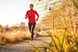 © Cavan Images - A woman running in an urban park on a bright autumnal day.