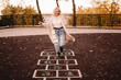 © Cavan Images - Young woman playing hopscotch in park during autumn