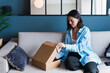 © Westend61 - Young woman opening package on sofa at home
