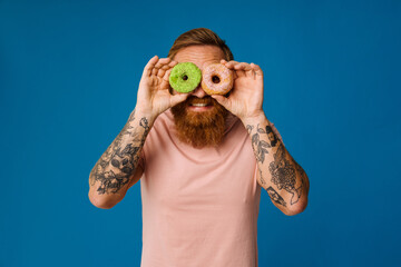 Wall Mural - Bearded man holding donuts while standing isolated over blue background