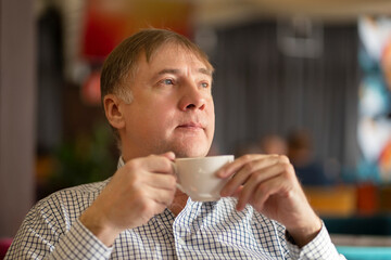 Serious face of a European, middle-aged man, over 50 years old with a tea mug in his hands, close-up. Portrait of a sad man in his fifties