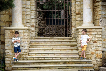 Wall Mural - Two little boys with modern haircuts near the stairs in colorful T-shirts and single tone pants. Concept of modern little boys